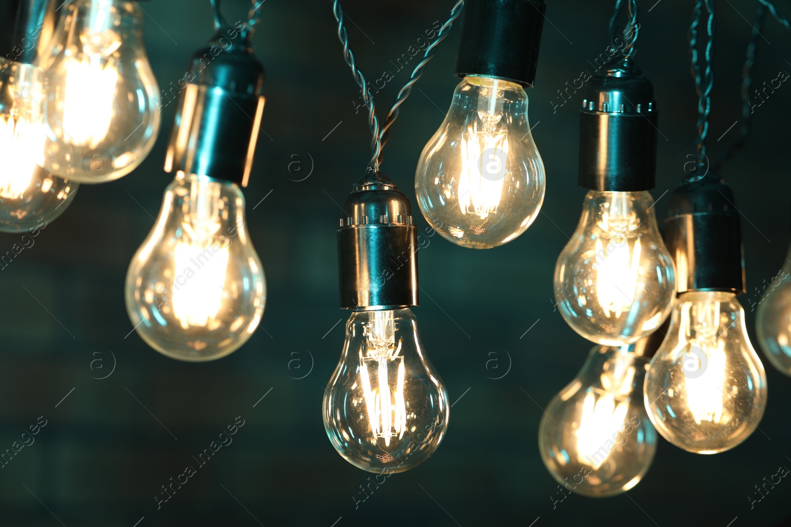 Photo of Glowing light bulbs hanging on color background, closeup