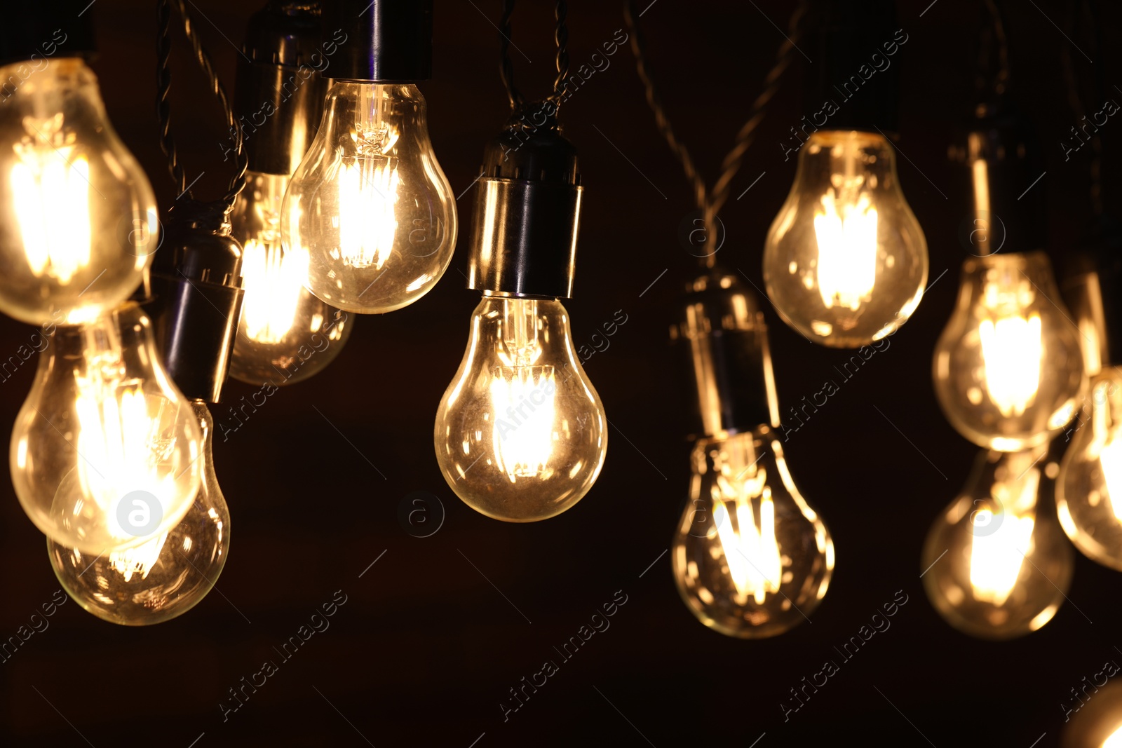 Photo of Glowing light bulbs hanging on dark background, closeup