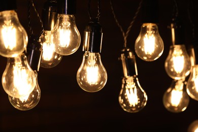 Photo of Glowing light bulbs hanging on dark background, closeup