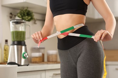 Photo of Weight loss. Woman measuring waist with tape in kitchen, closeup