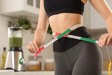 Photo of Weight loss. Woman measuring waist with tape in kitchen, closeup