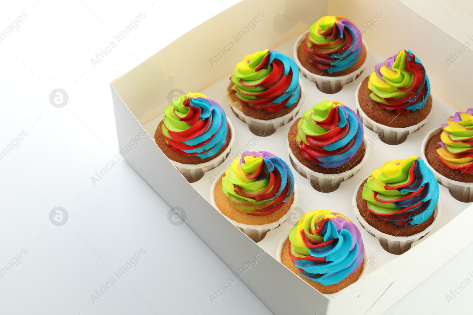 Photo of Tasty cupcakes with colorful cream in box on white background