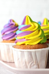 Photo of Tasty cupcakes with colorful cream on plate, closeup