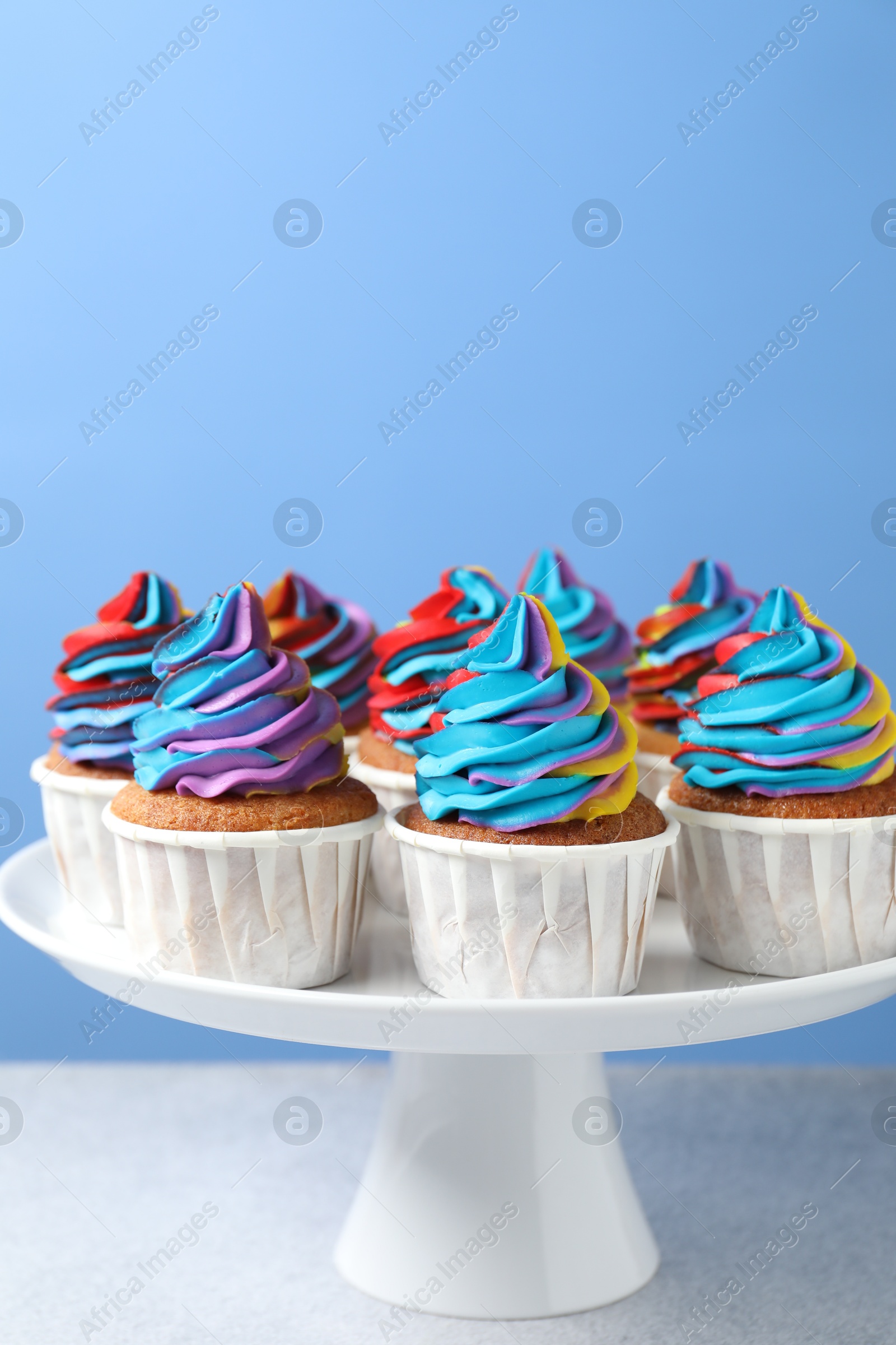 Photo of Tasty cupcakes with colorful cream on white table against light blue background, closeup