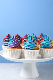 Photo of Tasty cupcakes with colorful cream on white table against light blue background, closeup