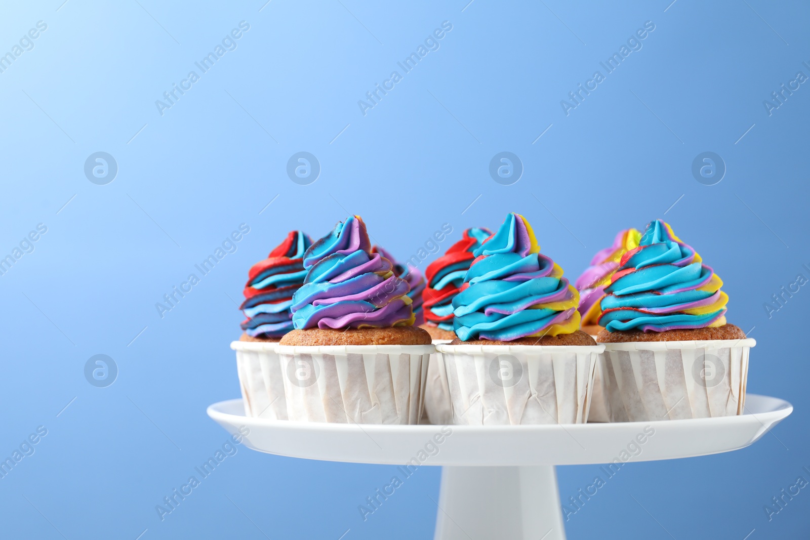 Photo of Tasty cupcakes with colorful cream on light blue background, closeup. Space for text