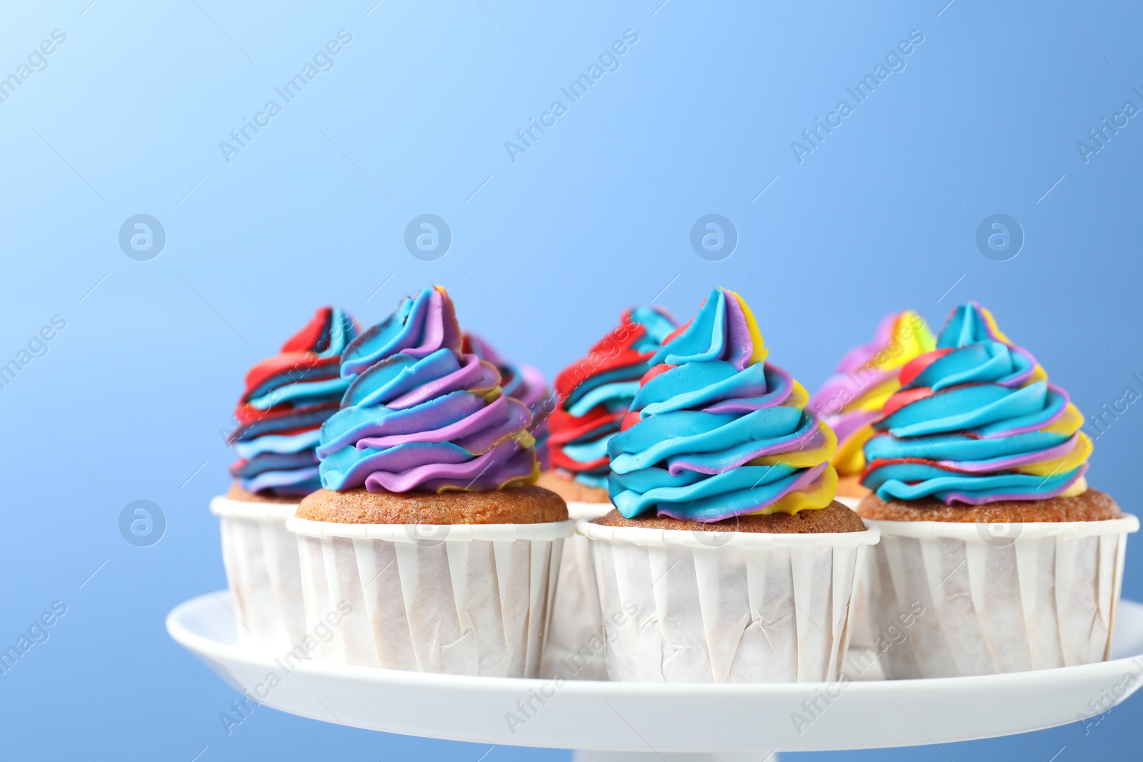 Photo of Tasty cupcakes with colorful cream on light blue background, closeup