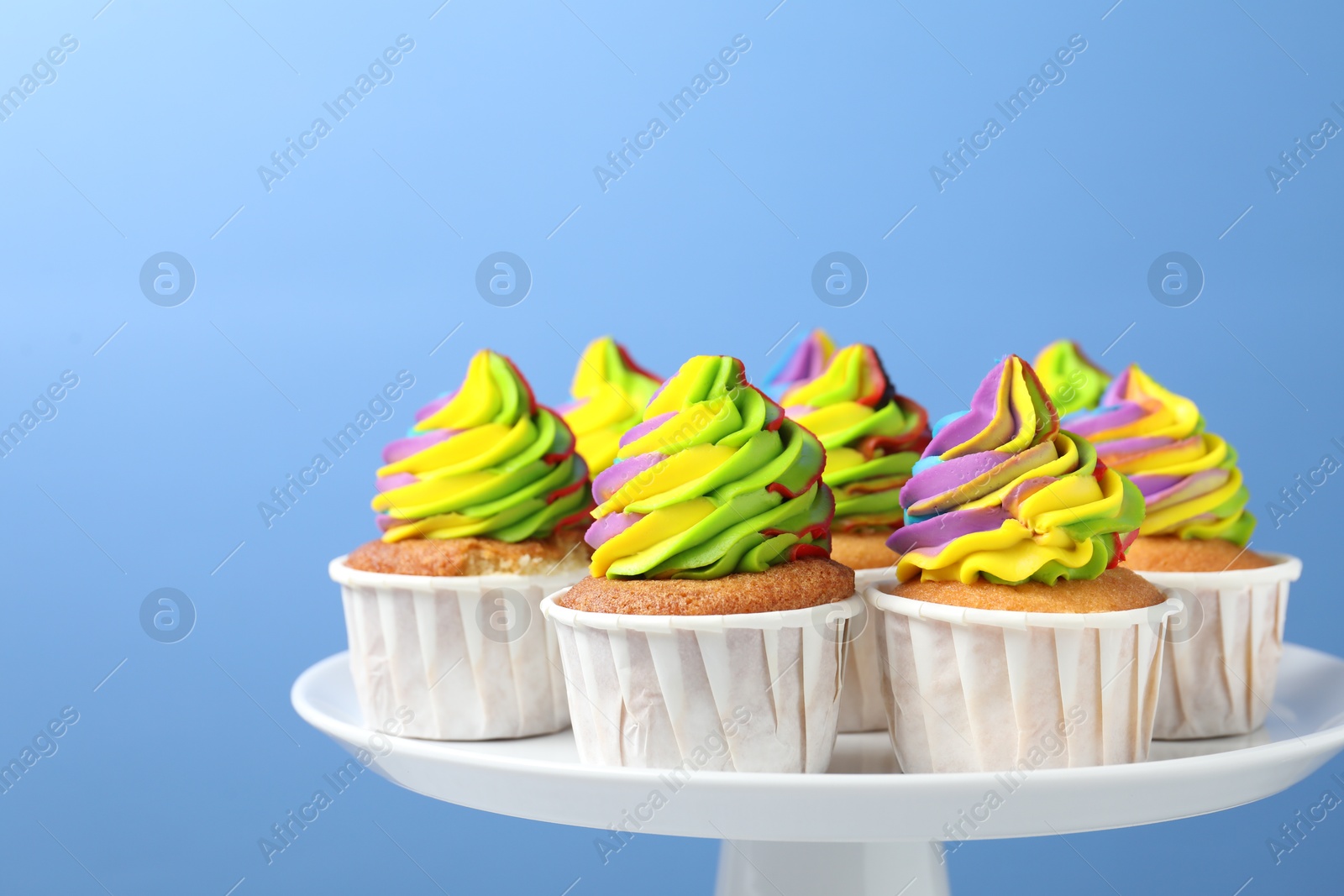 Photo of Tasty cupcakes with colorful cream on light blue background, closeup