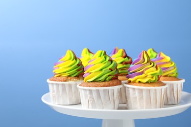 Photo of Tasty cupcakes with colorful cream on light blue background, closeup