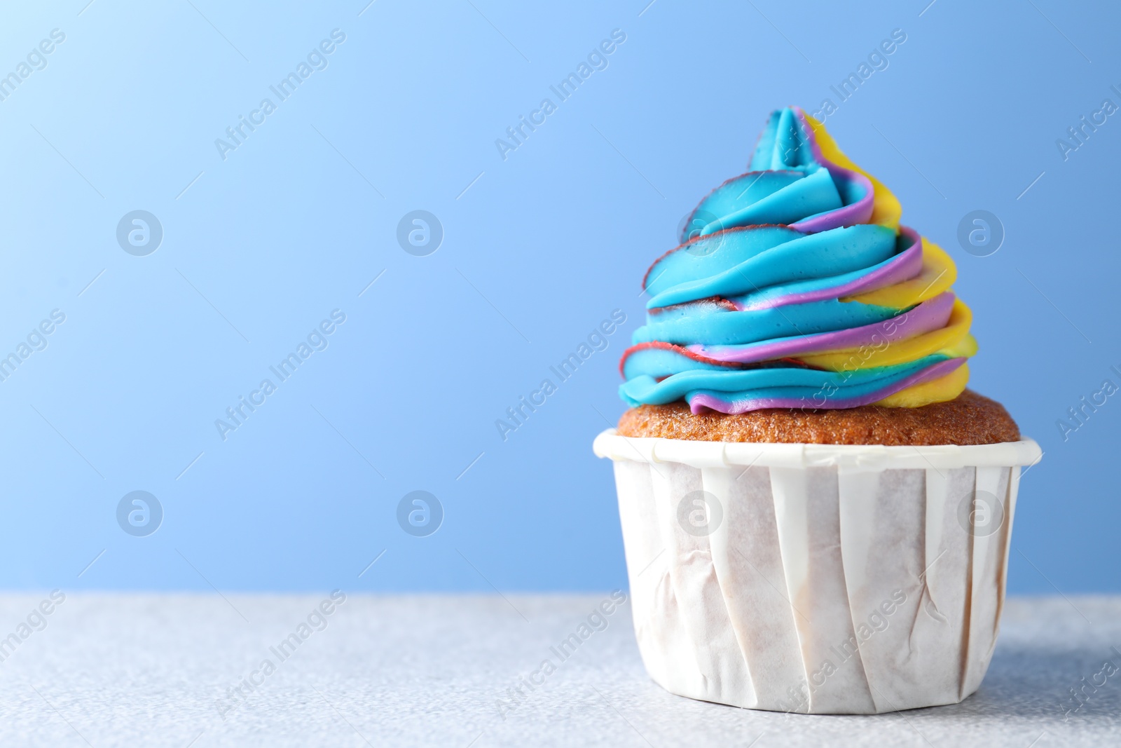 Photo of Tasty cupcake with colorful cream on white table against light blue background, closeup. Space for text