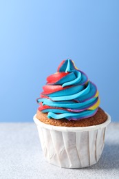 Photo of Tasty cupcake with colorful cream on white table against light blue background, closeup