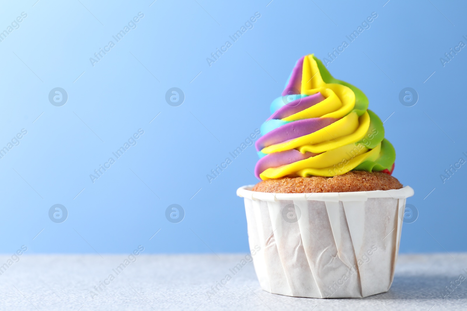 Photo of Tasty cupcake with colorful cream on white table against light blue background, closeup. Space for text