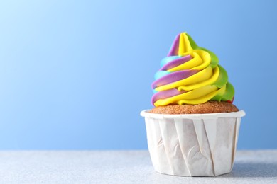 Photo of Tasty cupcake with colorful cream on white table against light blue background, closeup. Space for text