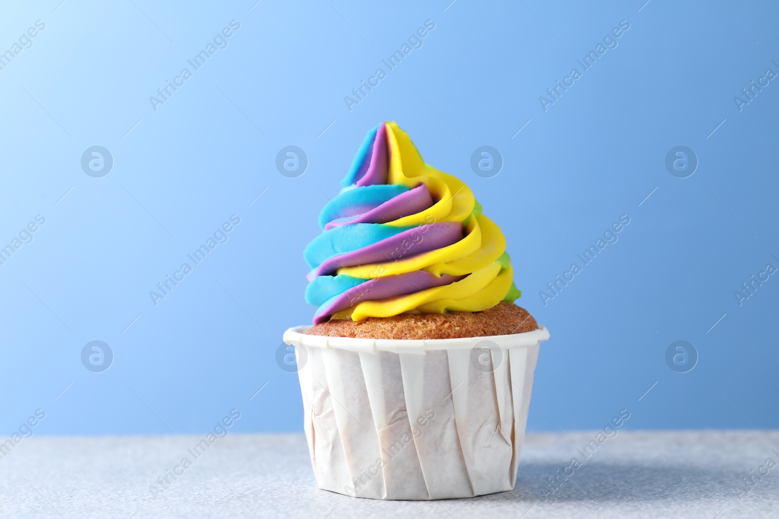 Photo of Tasty cupcake with colorful cream on white table against light blue background, closeup