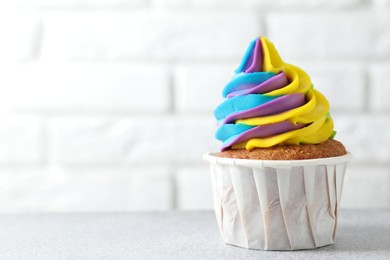 Photo of Tasty cupcake with colorful cream on white table, closeup. Space for text