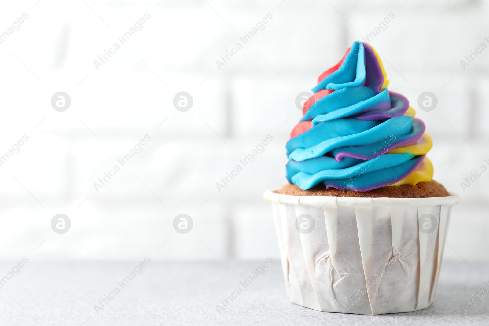 Photo of Tasty cupcake with colorful cream on white table, closeup. Space for text