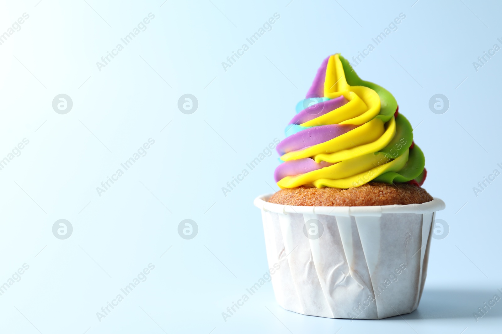 Photo of Tasty cupcake with colorful cream on light blue background, closeup. Space for text