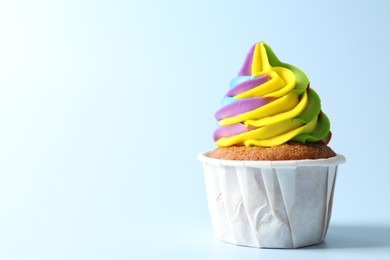 Photo of Tasty cupcake with colorful cream on light blue background, closeup. Space for text