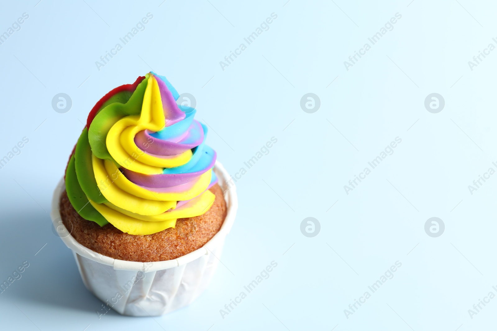 Photo of Tasty cupcake with colorful cream on light blue background, closeup. Space for text