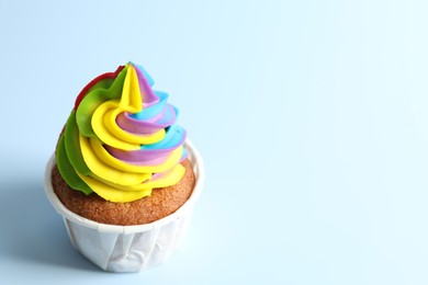 Photo of Tasty cupcake with colorful cream on light blue background, closeup. Space for text