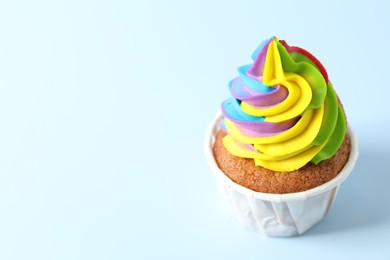 Photo of Tasty cupcake with colorful cream on light blue background, closeup. Space for text