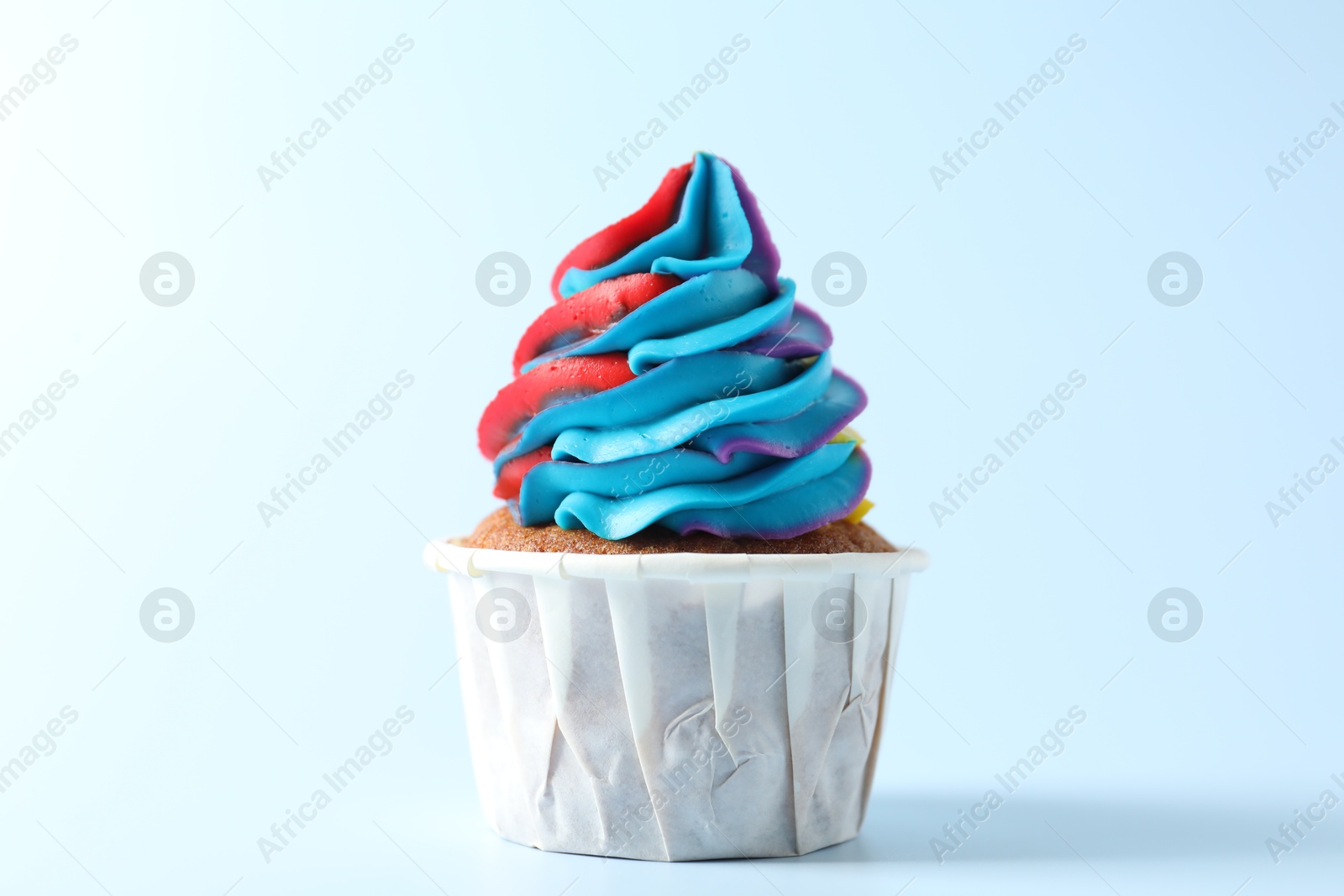 Photo of Tasty cupcake with colorful cream on light blue background, closeup