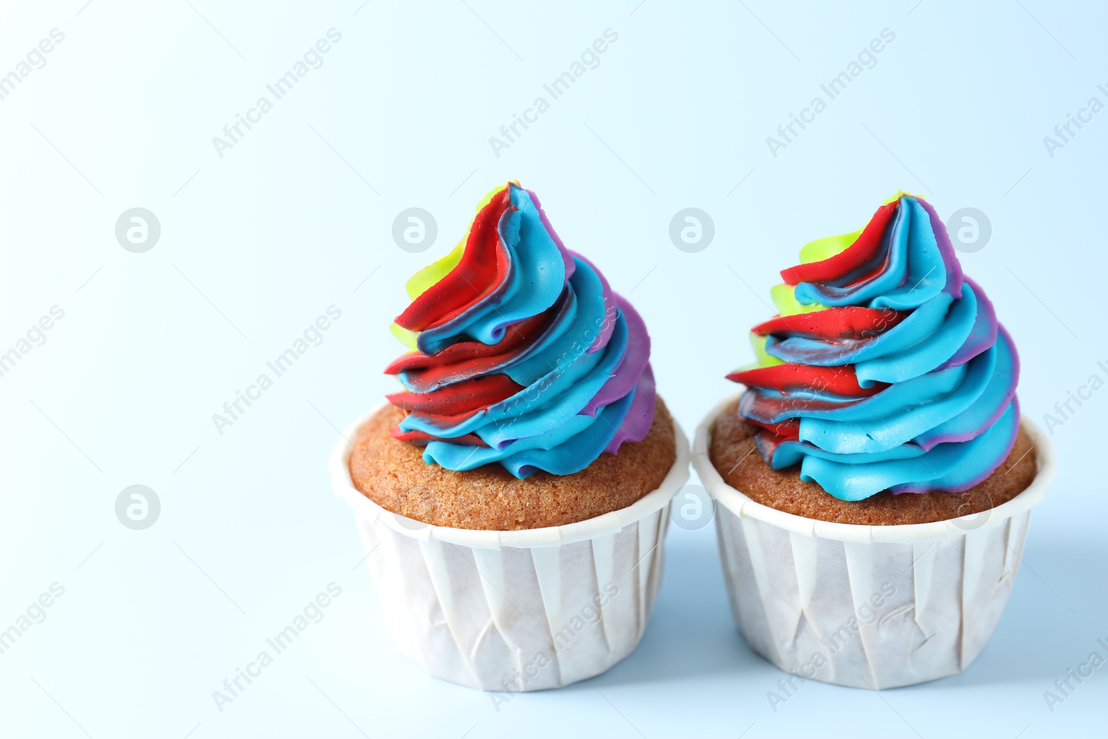 Photo of Tasty cupcakes with colorful cream on light blue background, closeup. Space for text