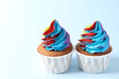 Photo of Tasty cupcakes with colorful cream on light blue background, closeup. Space for text