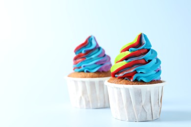 Photo of Tasty cupcakes with colorful cream on light blue background, closeup. Space for text