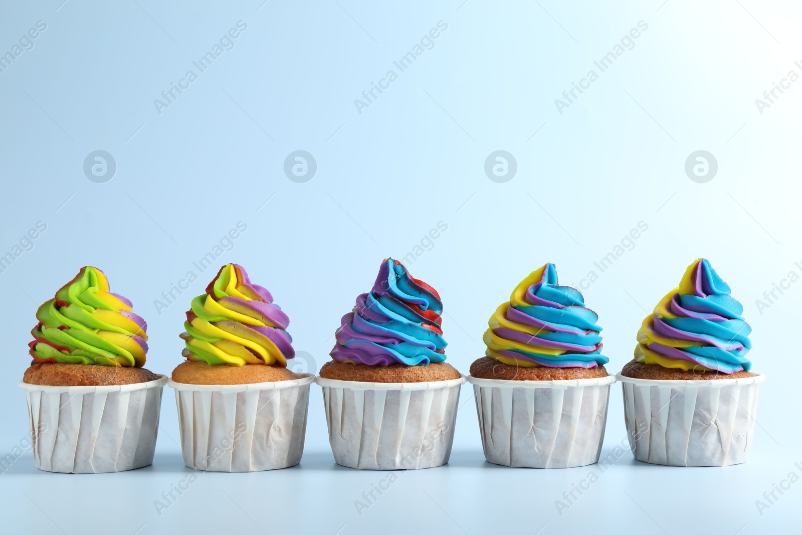 Photo of Tasty cupcakes with colorful cream on light blue background, space for text