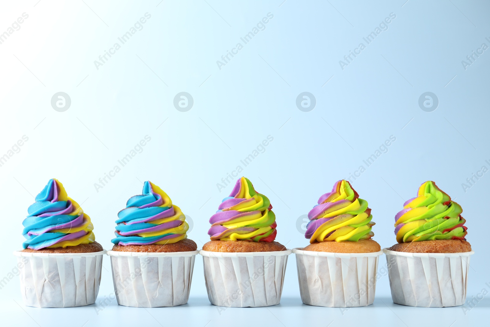 Photo of Tasty cupcakes with colorful cream on light blue background, space for text