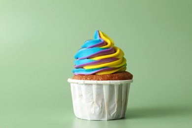 Photo of Tasty cupcake with colorful cream on light green background, closeup