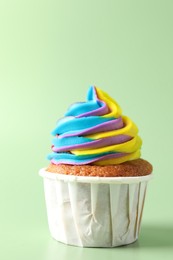 Photo of Tasty cupcake with colorful cream on light green background, closeup