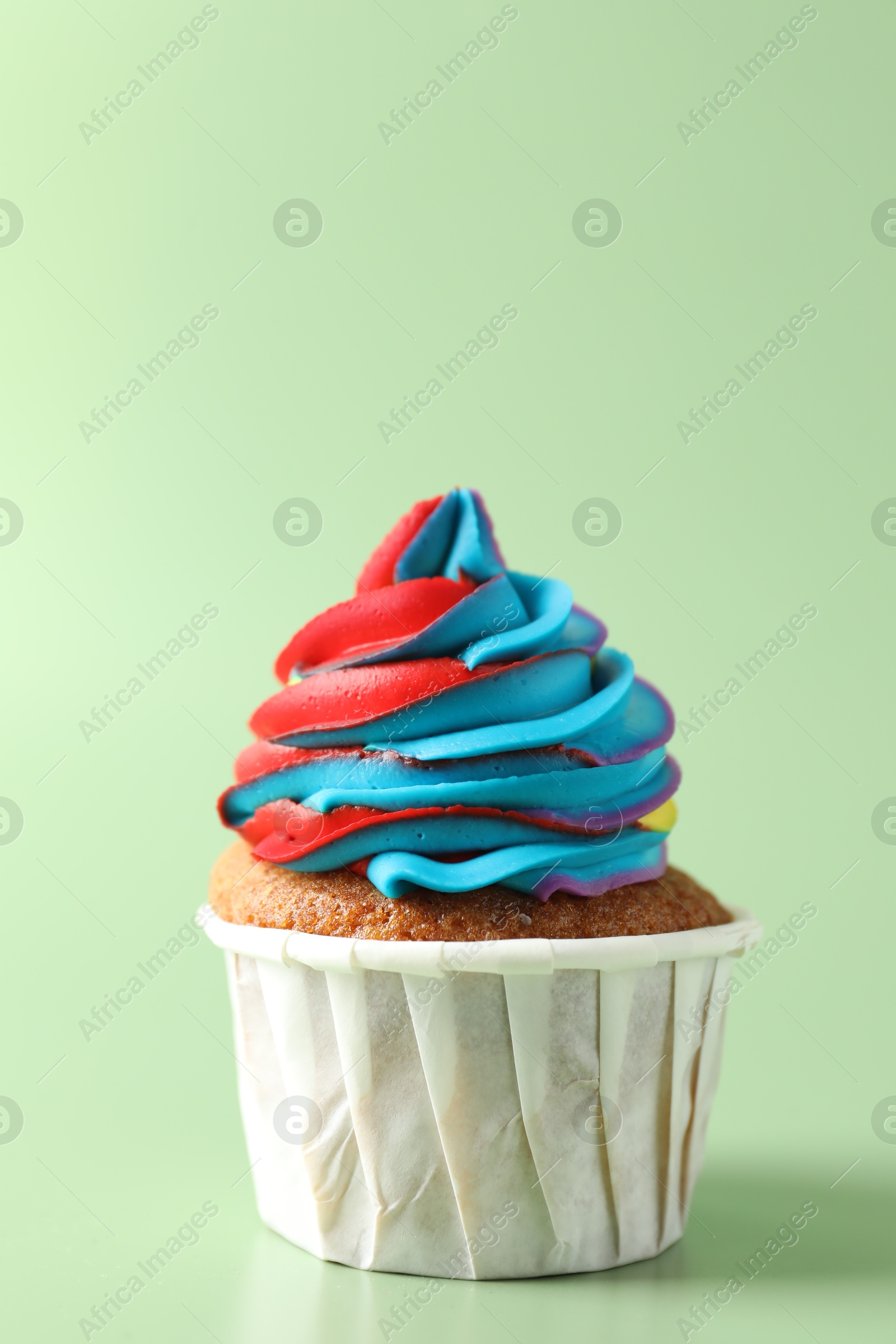 Photo of Tasty cupcake with colorful cream on light green background, closeup