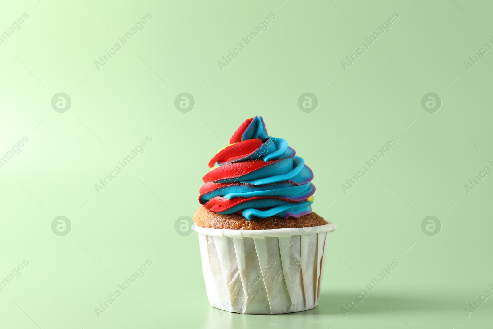 Photo of Tasty cupcake with colorful cream on light green background, closeup