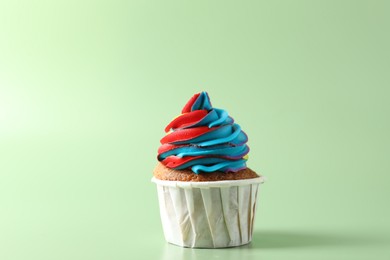 Photo of Tasty cupcake with colorful cream on light green background, closeup