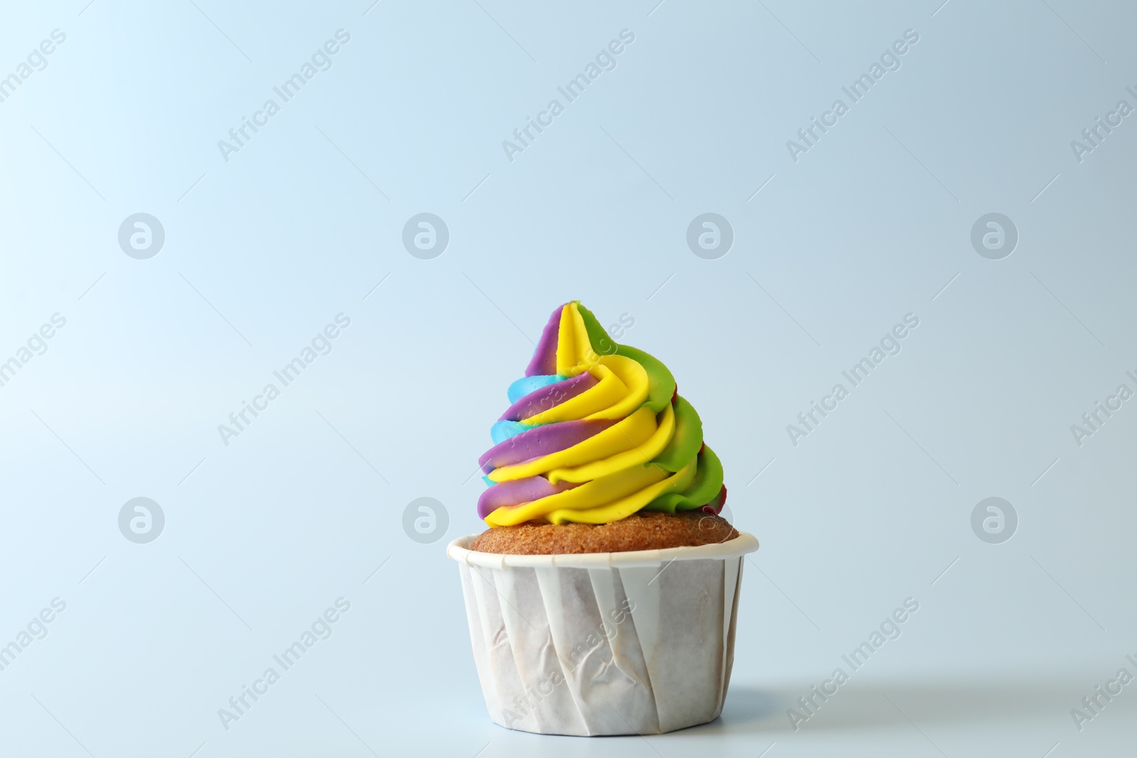 Photo of Tasty cupcake with colorful cream on light blue background