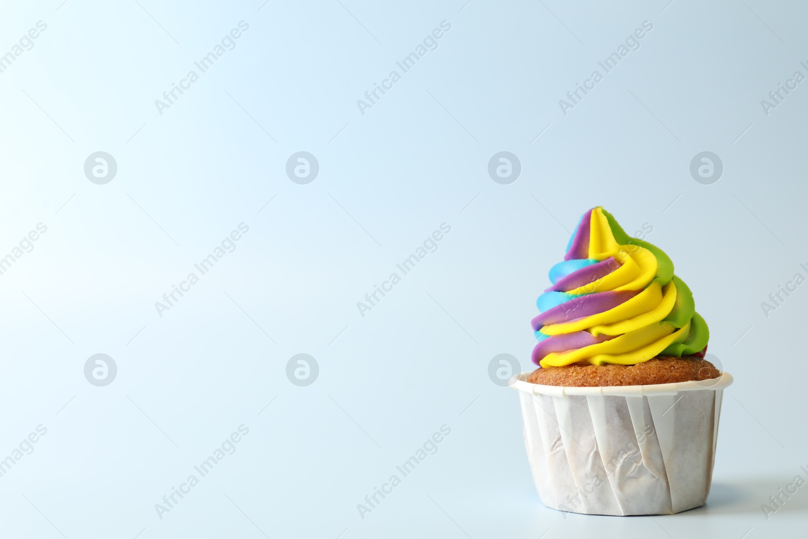 Photo of Tasty cupcake with colorful cream on light blue background, space for text