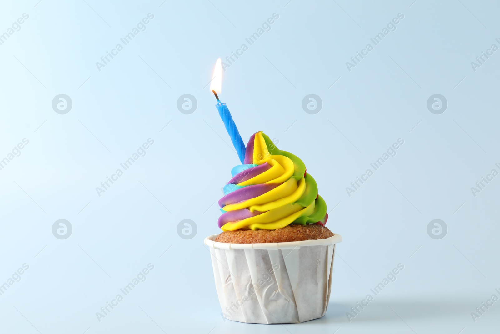 Photo of Tasty cupcake with colorful cream and burning candle on light blue background