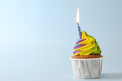 Photo of Tasty cupcake with colorful cream and burning candle on light blue background, space for text