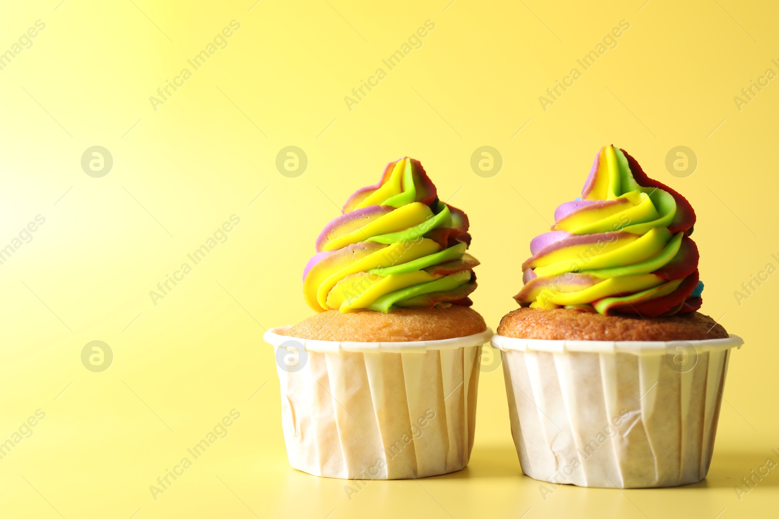 Photo of Tasty cupcakes with colorful cream on yellow background, closeup. Space for text