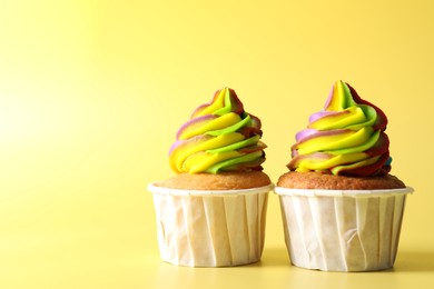 Photo of Tasty cupcakes with colorful cream on yellow background, closeup. Space for text