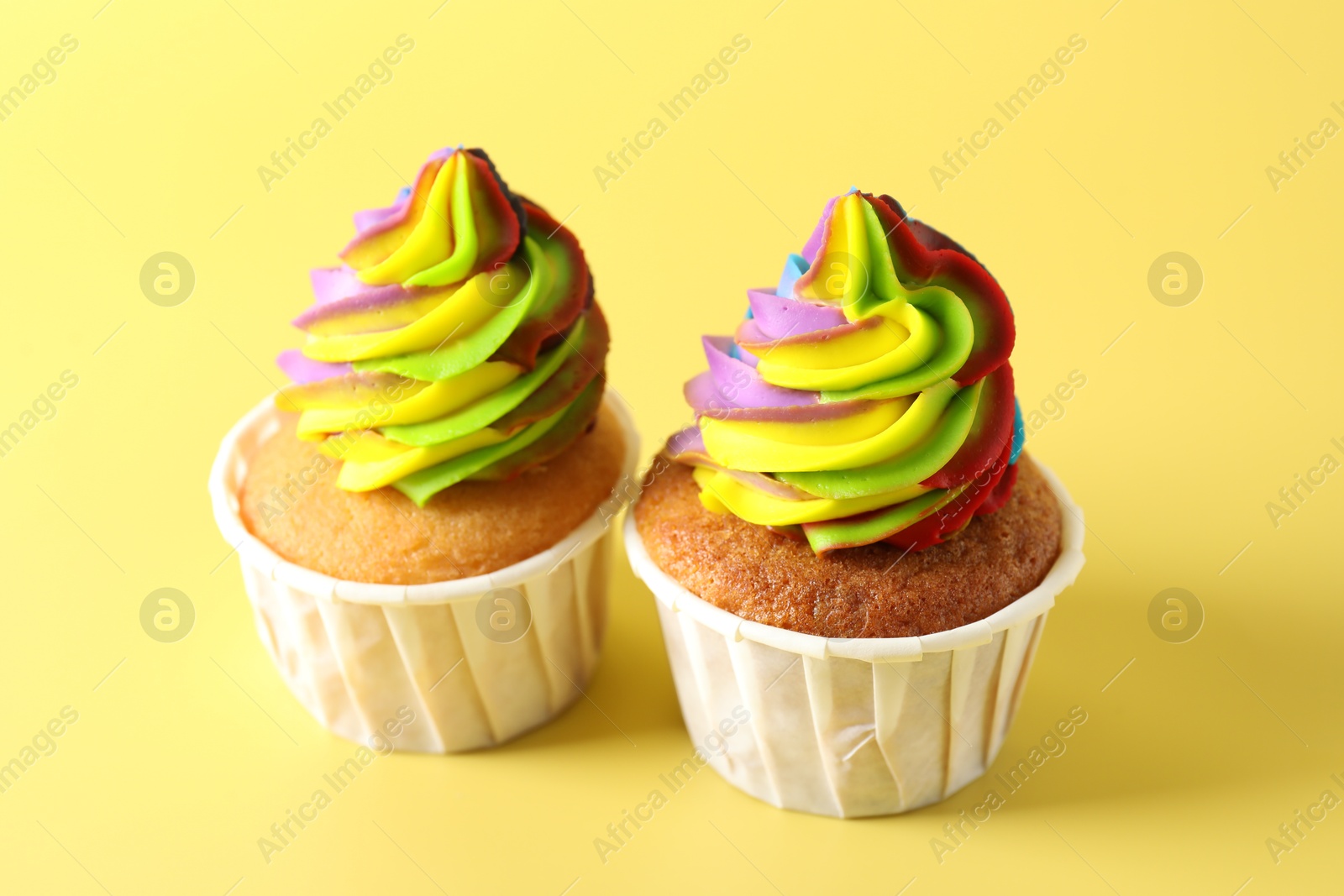 Photo of Tasty cupcakes with colorful cream on yellow background, closeup