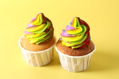 Photo of Tasty cupcakes with colorful cream on yellow background, closeup