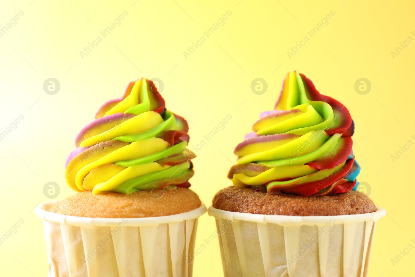 Photo of Tasty cupcakes with colorful cream on yellow background, closeup