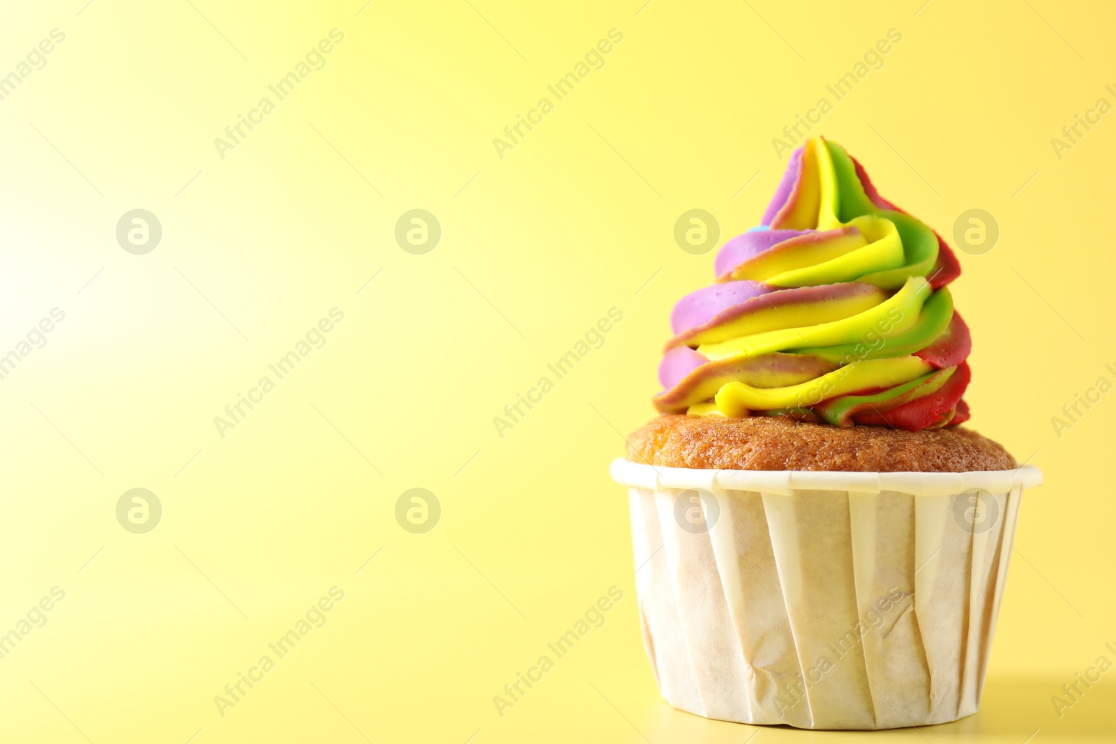 Photo of Tasty cupcake with colorful cream on yellow background, closeup. Space for text