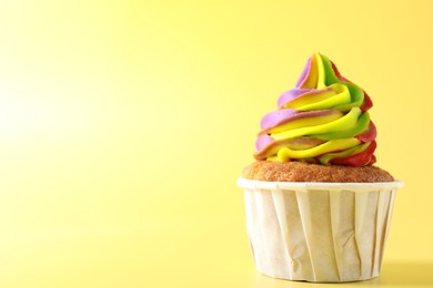 Photo of Tasty cupcake with colorful cream on yellow background, closeup. Space for text