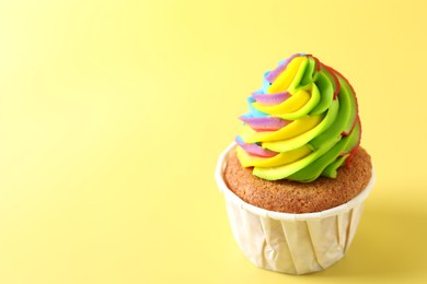 Photo of Tasty cupcake with colorful cream on yellow background, closeup. Space for text