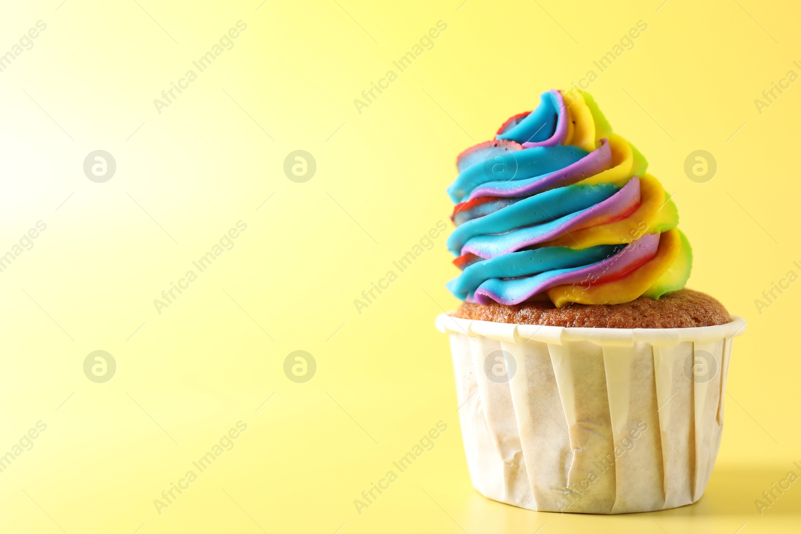 Photo of Tasty cupcake with colorful cream on yellow background, closeup. Space for text