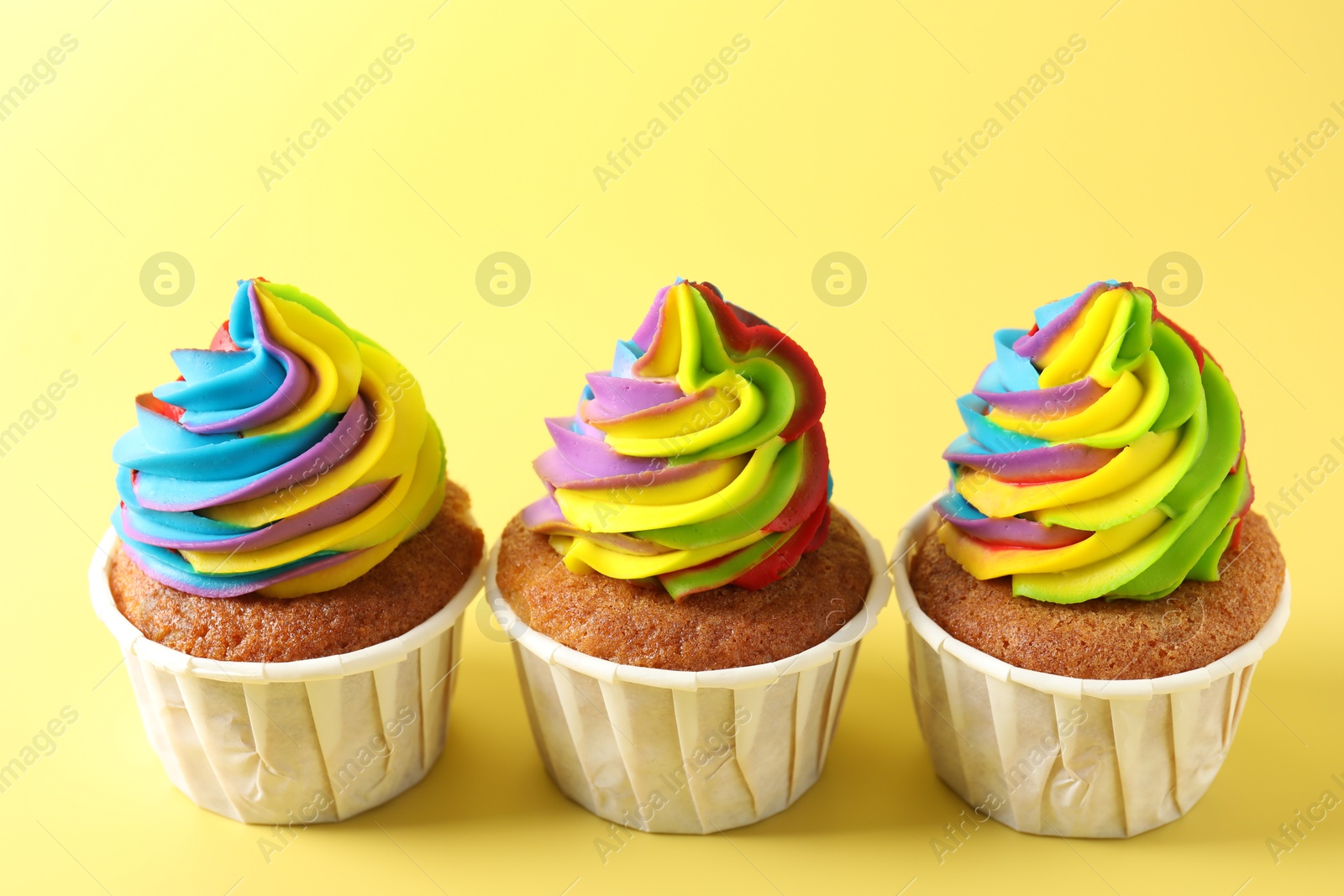 Photo of Tasty cupcakes with colorful cream on yellow background, closeup